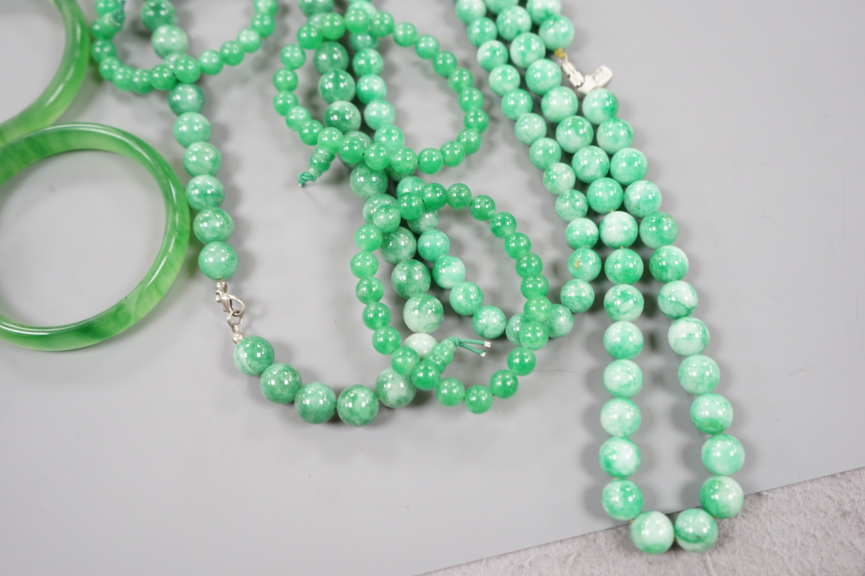 A group of three jadeite necklaces, together with two jadeite bracelets, two green glass bangles and a glass figure of a duck (8)